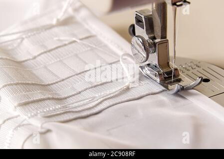 Ein Arbeiter arbeitet an einer Nähmaschine. Näherin näht weiße Vorhänge, Nahaufnahme. Stockfoto