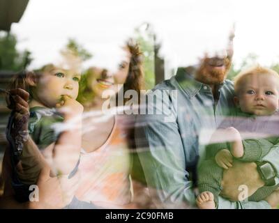 Familie mit Kindern (6-11 Monate, 2-3), die durch das Fenster schauen Stockfoto