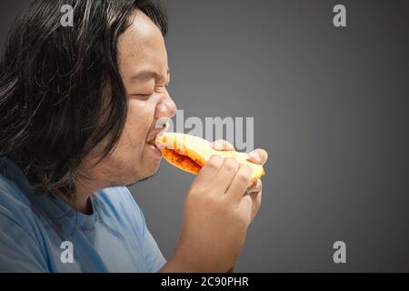 Asiatische Mann Essen Sandwich mit einem schwarzen Hintergrund. Junk-Food-Konzept Stockfoto