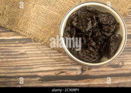Getrocknete Pflaumen in einer Metallschale auf einem Holzhintergrund. Nahaufnahme Stockfoto