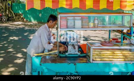 Sihanoukville, Kambodscha - 6. März 2012. Ein Straßenhändler läuft einen Stängel Zuckerrohr durch eine Presse, um frisch gepressten Saft, ein beliebtes Süßgetränk, zu machen. Stockfoto