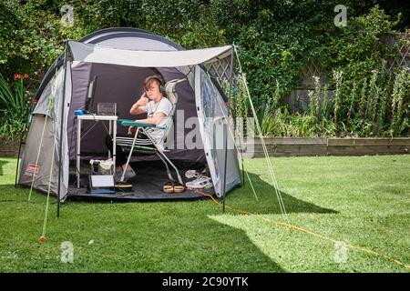 Ein Jugendlicher gibt den Daumen nach oben Zeichen, als er in einem Garten im Hintergrund während der Coronavirus-Krise, Juli 2020, campt. Stockfoto