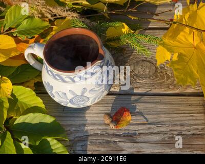 Herbst Stillleben, heißer Räuchertee in rustikal weiß blau bemalter Keramik Tasse mit bunten Herbstfarben Blätter, Buche und Ahornbaum Äste und Eiche Stockfoto