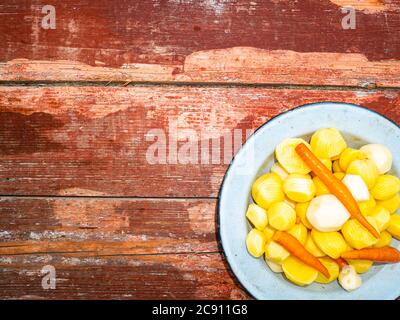 Geschälte Kartoffeln und Karotten in einer Schale auf einem Holztisch. Stockfoto