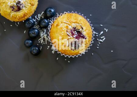 Blaubeer- und Kokosnussmuffins mit Zutaten, Blick von oben auf dunklem Schiefer. Hausgemachtes Backen. Stockfoto
