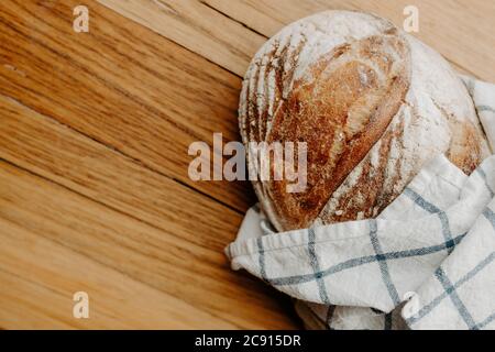 Hausgemachte Sour Teig Brot Kühlung auf einem Geschirrtuch, das auf einem hölzernen Schneidebrett mit Platz für Kopie Platz ist Stockfoto