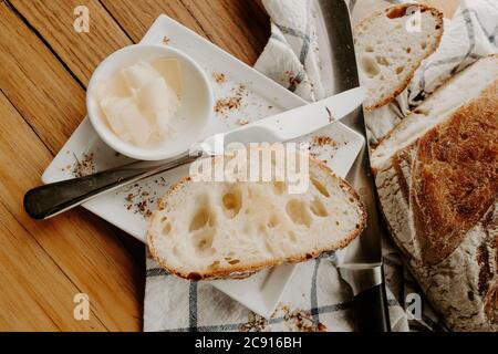 Krume, Kohlenhydrate, Backbrot, Mittagessen, Küchentisch, Authentisch, Nahaufnahme, gebuttert, knusprig, Brot, Sauerteig auf Holztisch, handwerklicher Bäcker Stockfoto