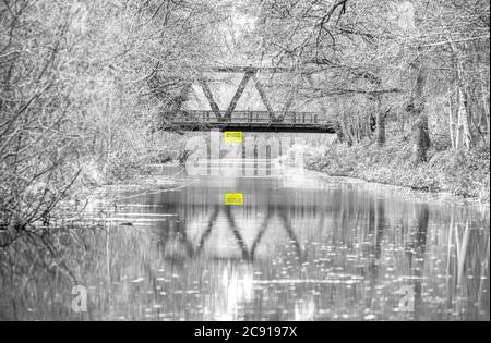 Eine alte Metallbrücke spiegelt sich in den stillen Gewässern des schönen Basingstoke Canal in diesem Foto, das an einem Winternachmittag in Hampshire aufgenommen wurde Stockfoto