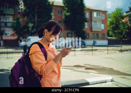 Attraktive Touristen mit einem Rucksack auf einer Stadtstraße mit einem Handy in den Händen. Seitenansicht einer Frau, die sich während des Aufenthalts auf einen Smartphone-Bildschirm konzentriert Stockfoto