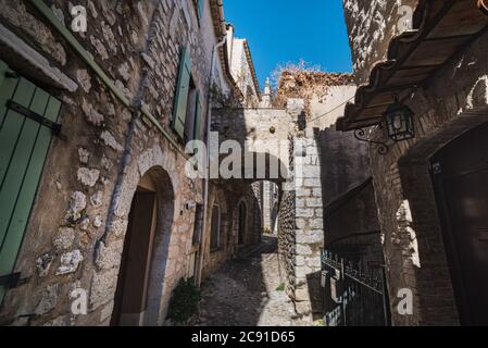 Eine gepflasterte Straße mit einem Steinbogen und trockenem Gras zeigt, wie es in einem mittelalterlichen Dorf - Saint Paul de Vence, Frankreich - ausgesehen haben muss Stockfoto