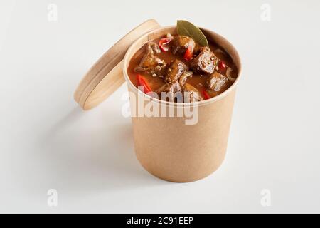 Generisches, unbeschriftetes Bottich mit Rindereintopf zum Mitnehmen, Gulasch oder Ragout mit abgedecktem Deckel, das das zarte Fleisch in einer reichen Soße auf weißem Hintergrund enthüllt Stockfoto