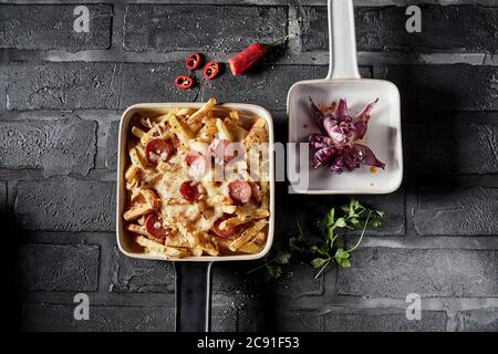 Goldene Pommes frites mit Käse und Salami, serviert mit einer roten Zwiebel in Form einer gebratenen Rosette in der Ansicht von oben auf einer schwarzen gekachelten Theke mit Copyspace Stockfoto