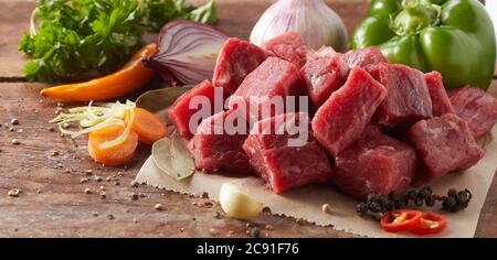 Gewürfeltes, rohes mageres Rindersteak für Gulasch mit einer Auswahl an gesundem Gemüse, Pfefferkörnern, Chilischoten und Knoblauch in Nahaufnahme Stockfoto