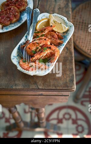 Gegrillte ganze rosa Garnelen gewürzt mit Gewürzen und Kräutern auf einer Steingutplatte mit Zitrone serviert auf einem rustikalen Tisch von oben gesehen Stockfoto