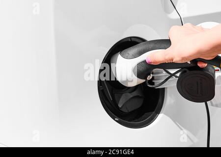 Nahaufnahme Womans Hand hält ein Ladegerät Stecker des Elektroautos. Emissionsfreies Fahrzeug Stockfoto