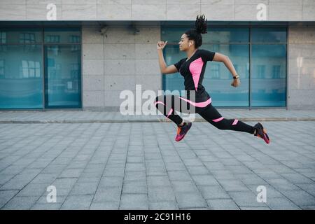 Übung für die Gewichtsabnahme. Frau in Sportkleidung mit kabellosen Kopfhörern, die in der Luft gefroren sind und beim Laufen springen Stockfoto