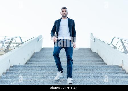 Lässige stilvolle junge Mann in Jacke und Jeans zu Fuß die Treppe hinunter, im Freien Stockfoto