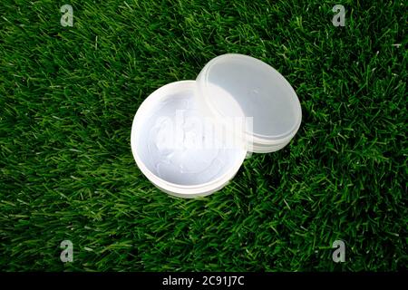 Schönheit, weißes Glas mit Körper Peeling auf grünem Gras Hintergrund close-up. Hautpflege Kosmetik. Stockfoto