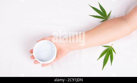 Beauty, Spa, Hautpflege Kosmetik mit Marihuana-Extrakt. Weißes Glas Creme in der Hand mit grünem Cannabisblatt auf weißem Hintergrund. Stockfoto