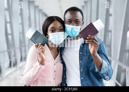 Sicher Reisen. Schwarzes Paar in medizinischen Masken posiert mit Pässen am Flughafen Stockfoto