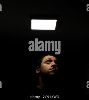 Junge kaukasische Mann unter dem quadratischen Licht in der Dunkles Zimmer Stockfoto