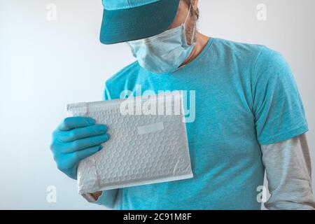 Lieferung Mann posiert mit Paket in Schutzkleidung tragen Baseball-Kappe, Schutzmaske und Handschuhe während Virusinfektion Pandemie outbre Stockfoto