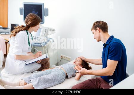 Vater hält die Hand der Tochter, während sie auf einer Couch liegt und mit einem Arzt spricht Stockfoto