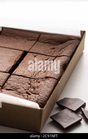 Nahaufnahme von köstlichen Brownie-Stücke in Karton in der Nähe von dunkler Schokolade auf weißem Hintergrund Stockfoto