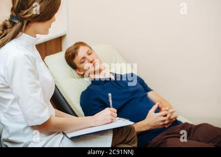 Der Arzt schreibt die Beschwerden ihres Patienten auf und hört ihm zu Stockfoto