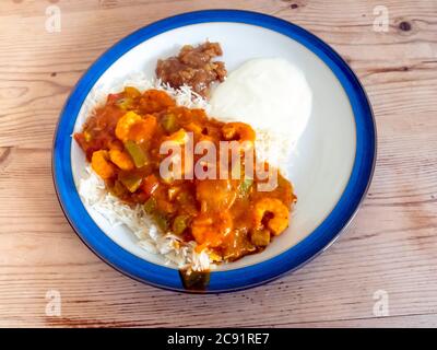 Indisches Essen Garnelen Curry Jalfrezi auf Basmati-Reis mit Joghurt und Mango-Chutney auf einer Holztischplatte Stockfoto