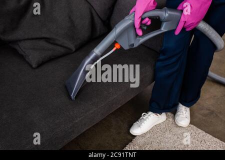 Abgeschnittene Ansicht des Staubsaugers in Gummihandschuhen, die den Staubsauger in der Nähe des Behandlungstisches halten Stockfoto