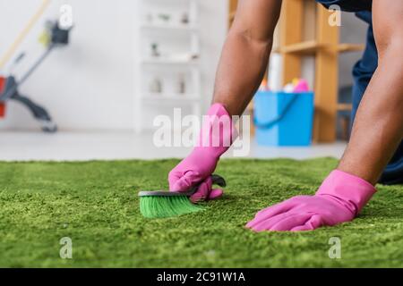 Beschnittene Ansicht der afroamerikanischen Reiniger in Gummihandschuhen Reinigung Teppich mit Bürste im Büro Stockfoto