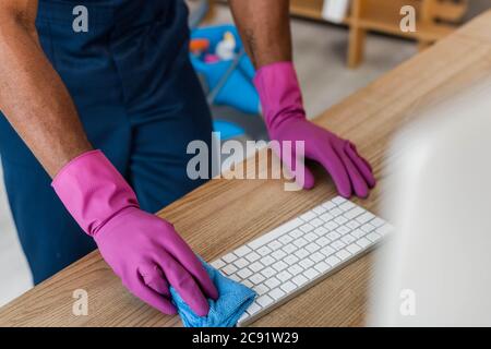 Beschnittene Ansicht der afroamerikanischen Reiniger in Gummihandschuhen Reinigung Computer-Tastatur im Büro Stockfoto