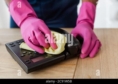 Beschnittene Ansicht der afroamerikanischen Reiniger in Gummihandschuhen Reinigung Telefon mit Lappen auf Tisch im Büro Stockfoto