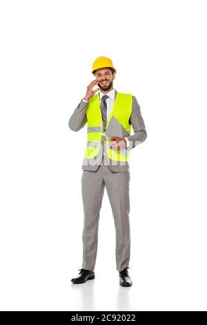 Lächelnder Techniker im Anzug, der auf dem Smartphone spricht und den Laptop auf weißem Hintergrund hält Stockfoto