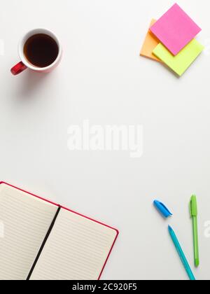 Draufsicht auf ein offenes rotes Notizbuch, farbige Erinnerungen, blauer und grüner Stift, eine rote Tasse Kaffee auf weißem Hintergrund, mit Platz für Text in der Mitte Stockfoto