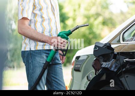 Beschnittene Ansicht des Mannes, der die Kraftstoffdüse in der Nähe des Autos mit offener Tankabdeckung im Freien hält Stockfoto