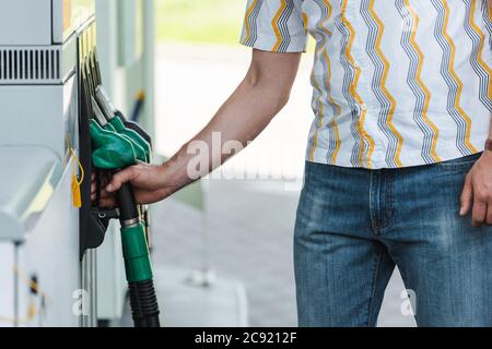 Beschnittene Ansicht des Mannes, der die Zapfpistole an der Tankstelle im Freien hält Stockfoto