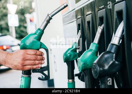 Beschnittene Ansicht des Mannes, der die Zapfpistole an der Tankstelle auf der Stadtstraße hält Stockfoto