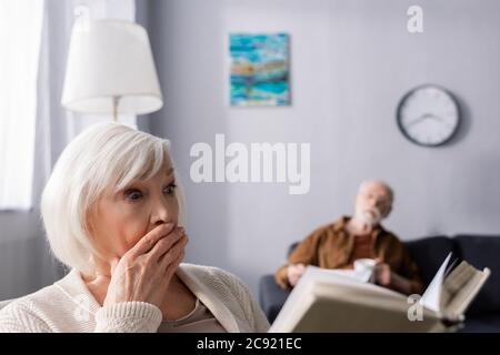 Selektive Konzentration des älteren Mannes auf schockierte Frau Buch lesen Stockfoto