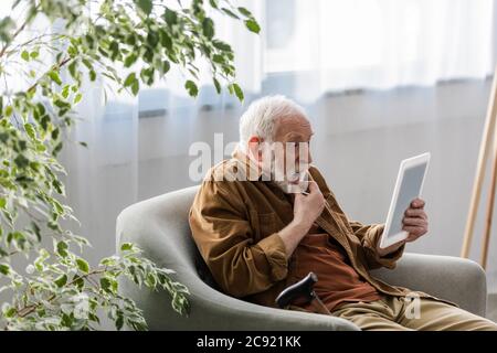 Schockiert Senior Mann mit digitalen Tablet, während im Sessel sitzen Stockfoto