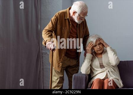 Älterer Mann mit Gehstock, der neben der an Hedache leidenden Frau steht Stockfoto