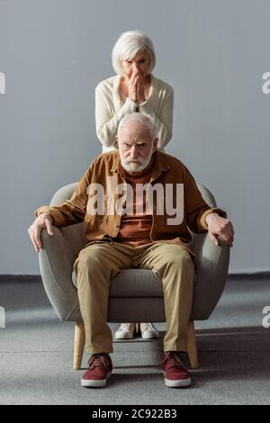 Geschockte ältere Frau, die ihr Gesicht berührte, während sie hinter ihrem Mann stand, krank an Demenz Stockfoto