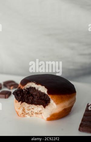 Vertikale Aufnahme eines gebissenen Boston Creme Donut mit einem Schokoladenfüllung auf weißem Hintergrund Stockfoto