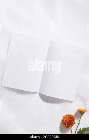 Draufsicht auf Voile Stoff Hintergrund mit zwei orangen Blumen und ein Stück weißes Papier mit Platz für Text. Vertikal Stockfoto