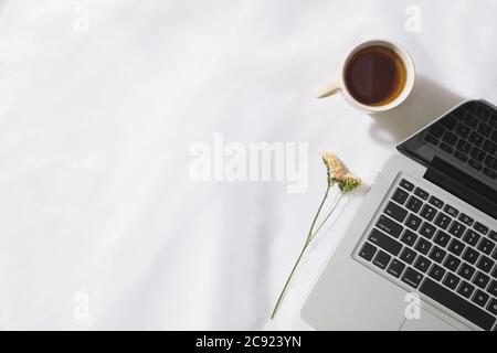 Draufsicht auf Morgentee in Voile Stoff Hintergrund mit einem Laptop, Tasse Tee und eine Blume mit Platz für Text Stockfoto