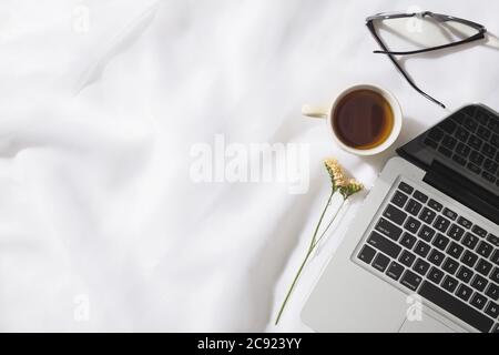 Draufsicht auf Morgentee in Voile Stoff Hintergrund mit einem Laptop, Tasse Tee, Gläser und eine Blume mit Platz für Text Stockfoto