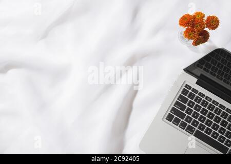 Draufsicht auf Voile Stoff Hintergrund mit einem Laptop, und eine Vase mit orangen Blumen mit Platz für Text Stockfoto
