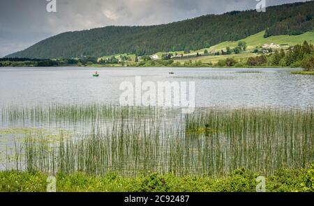 Der Rousses See mit Gras und Fischern. Wir sehen den Fischer auf den Booten und den Berg auf dem Rücken Stockfoto