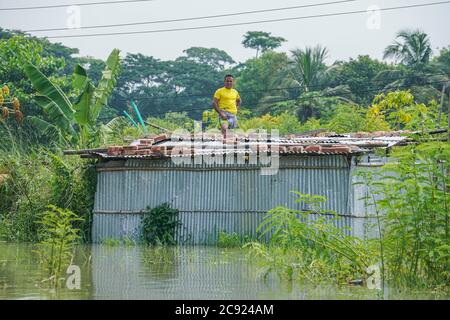 Munshiganj, Bangladesch. Juli 2020. Ein Mann steht auf dem Dach seines überfluteten Hauses in Sreenagar in Munshiganj bei Dhaka.ein Drittel von Bangladesch ist unter Wasser nach einigen der schwersten Regenfälle seit einem Jahrzehnt und mehr als 3 Millionen Menschen waren mit Häusern und Straßen in Dörfern überflutet betroffen, Beamte des Hochwasserprognosen- und Warnzentrums (FFWC) haben dies gesagt. Die Überschwemmungssituation in 20 nördlichen und zentralen Bezirken aufgrund des Anstiegs des Wasserstockels der Hauptflüsse, einschließlich der Brahmaputra, Jamuna, Padma, Teesta und Dharla. Kredit: SOPA Images Limited/Alamy Live Nachrichten Stockfoto